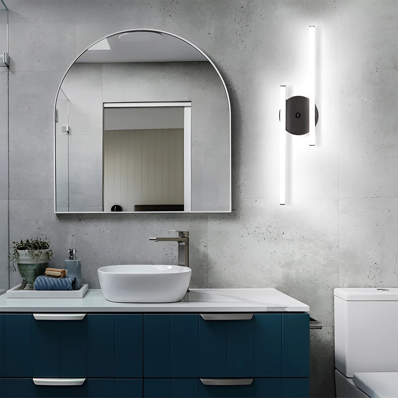 Dual-arm adjustable LED wall sconce in black with a modern minimalist design, providing natural light, installed above a bathroom sink with a mirror and cabinetry.