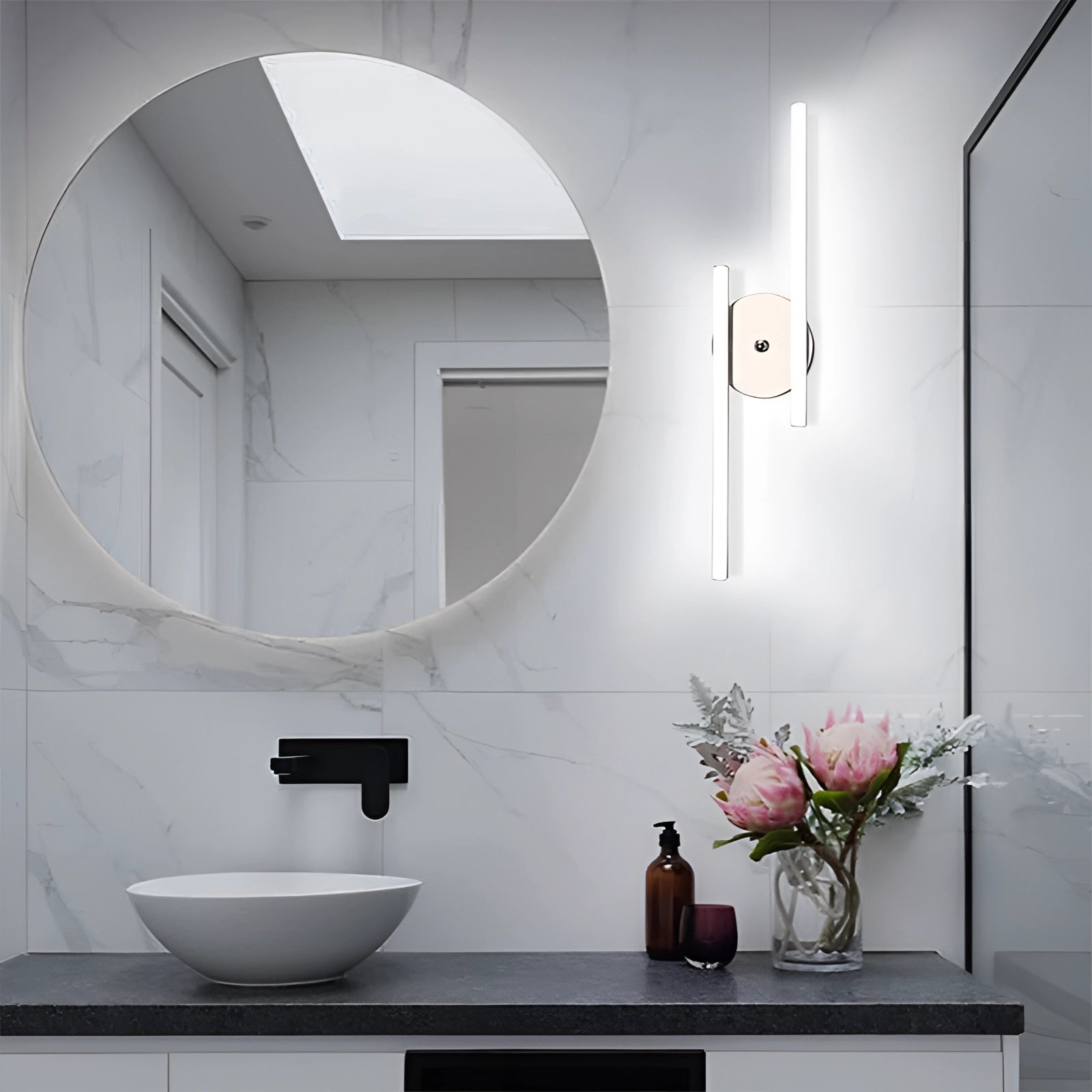 Dual-arm adjustable LED wall sconce in silver finish with a modern minimalist design, mounted above a bathroom sink with a mirror and a potted plant, emitting natural light in a contemporary bathroom setting.