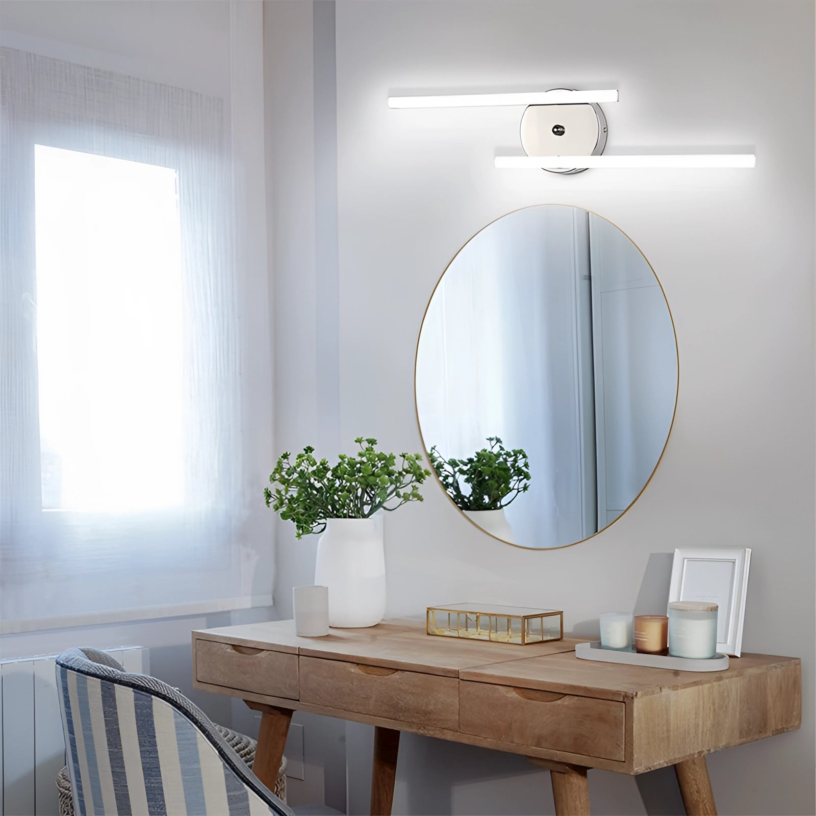 Modern minimalist dual-arm adjustable LED wall sconce mounted on a white wall in a stylish interior setting featuring wooden furniture, a table, a green potted plant, and a large rectangular mirror.