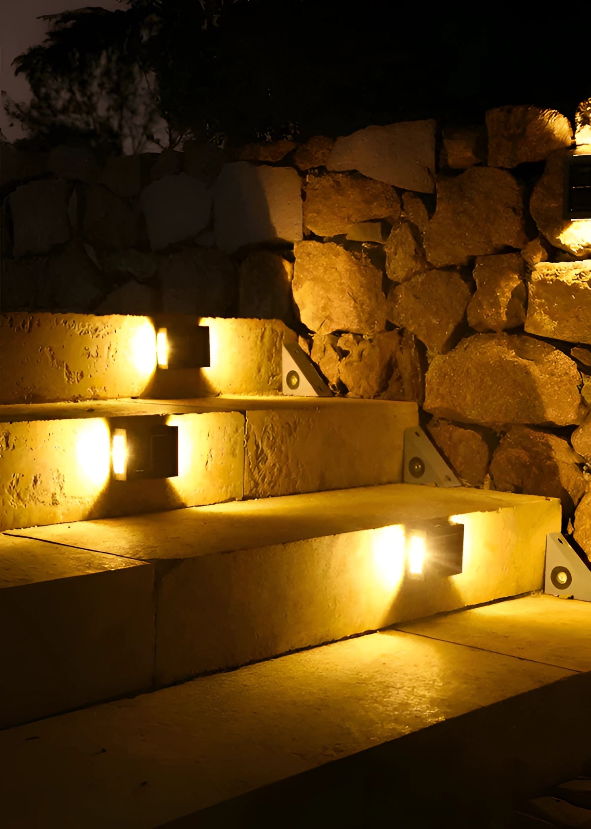 A solar outdoor lamp mounted on a wooden wall with an adjustable bracket, emitting a warm amber glow that illuminates the surrounding landscape in the darkness.