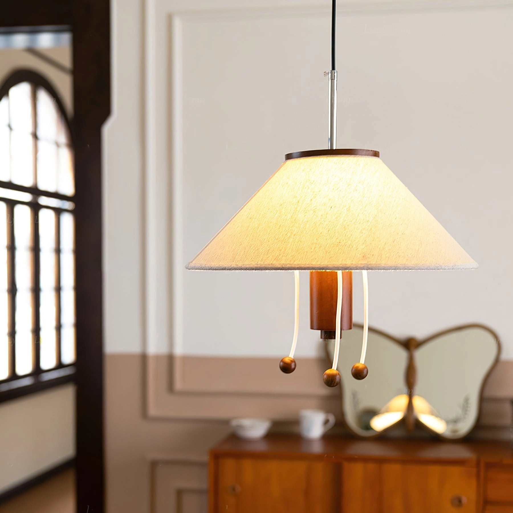 Elegant pendant lamp with modern wood detailing and a fabric shade, suspended in a stylish interior setting. The lamp radiates a warm light, enhancing the contemporary design elements of the room, including wooden shelves and a large window.