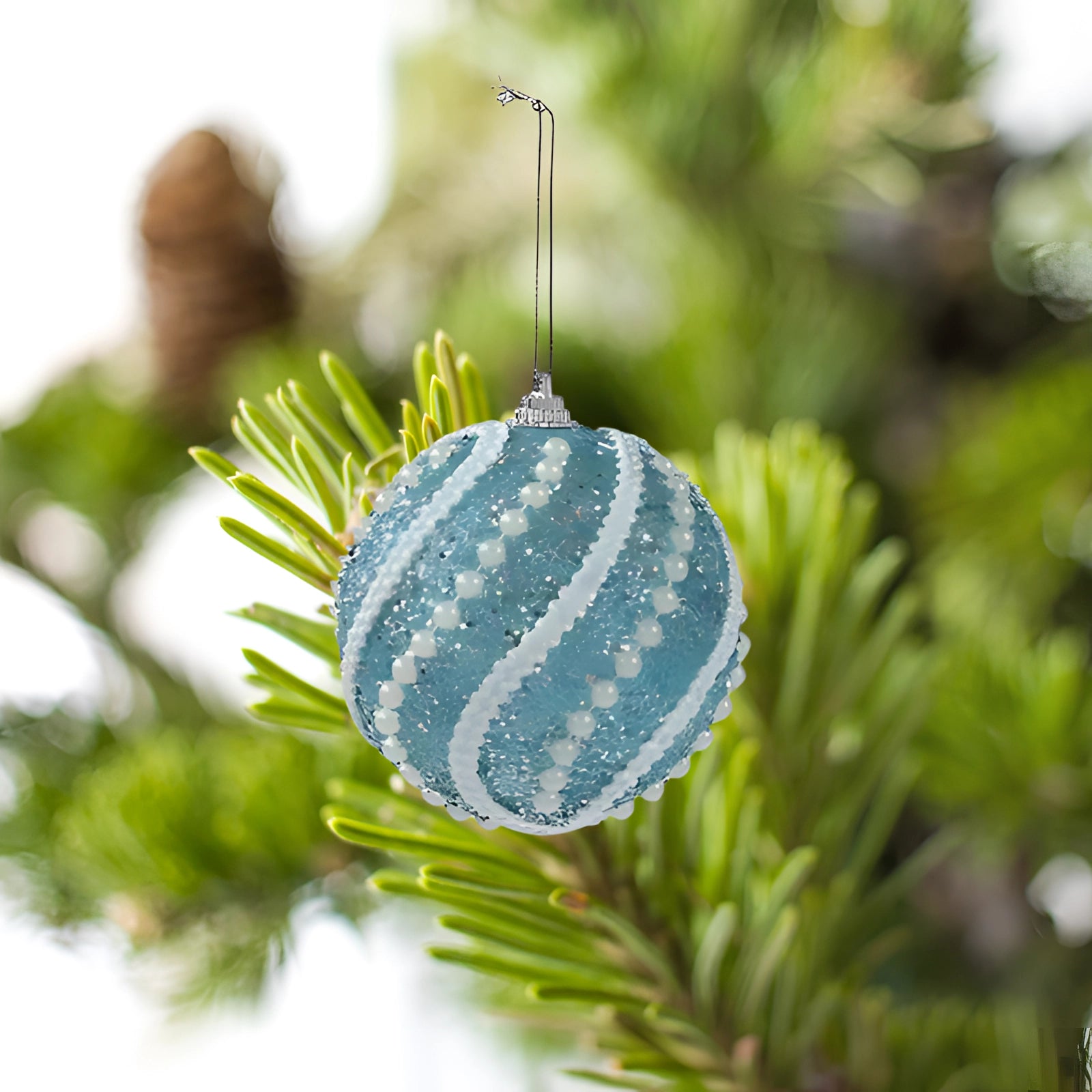 Elegant blue sequin Christmas ornament with a glittery finish, hanging on an evergreen Christmas tree branch, adding a festive sparkle to the holiday decor.