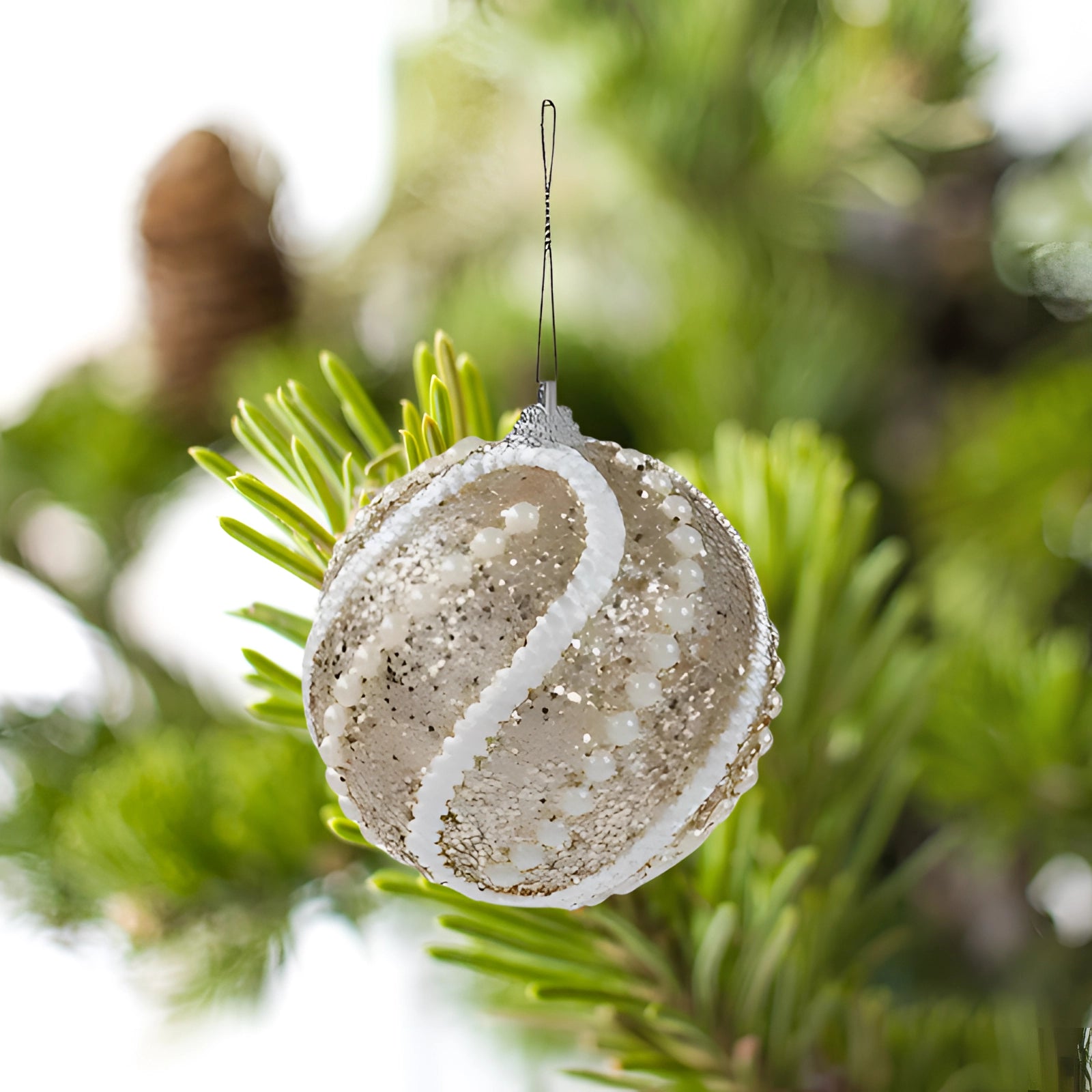 Elegant bronze sequin ornament in a spherical shape, resembling a Christmas bauble with a glittery texture, surrounded by evergreen foliage.