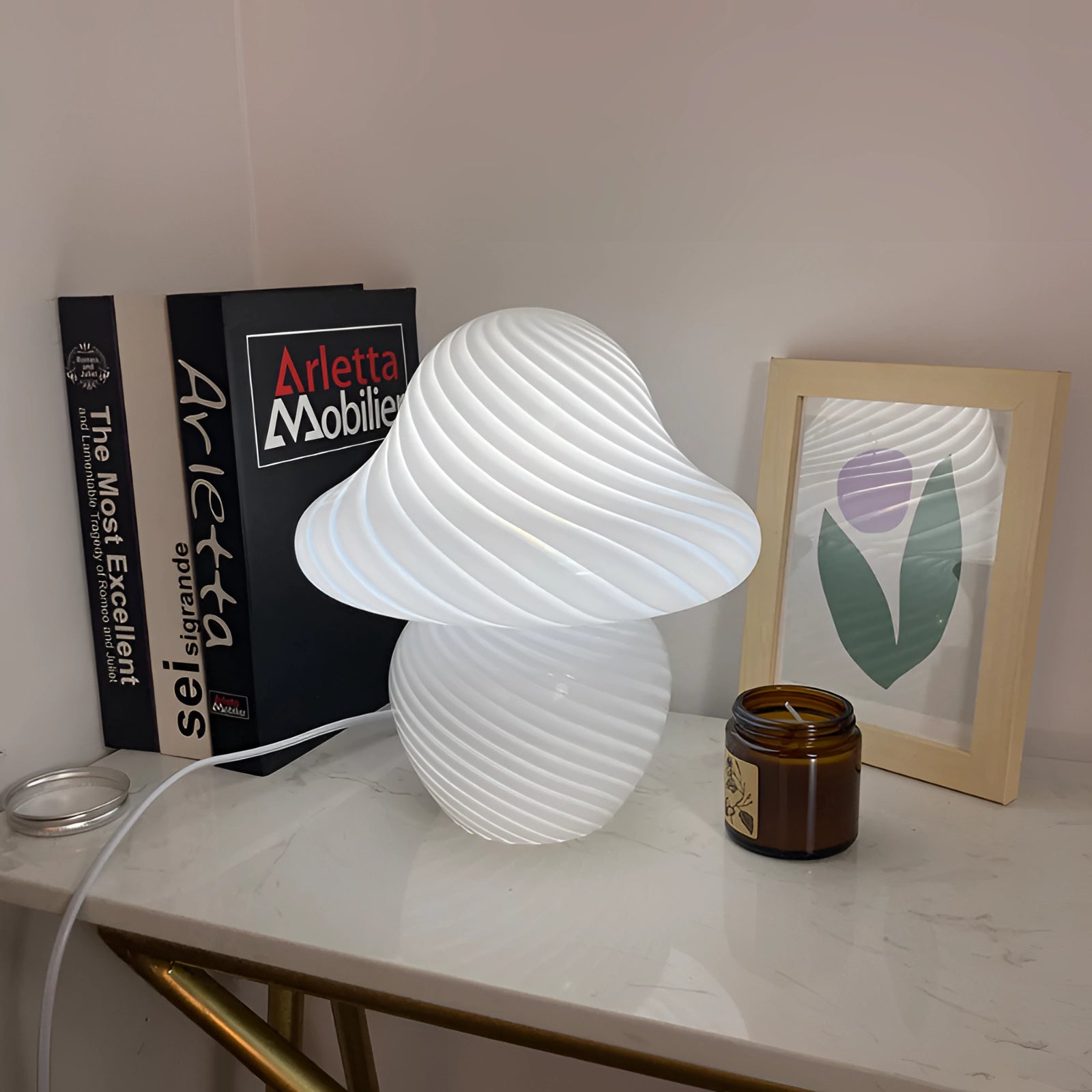 Elegant white spiral table lamp with a modern sculptural design placed on a wooden shelf, featuring a rectangular base and hardwood flooring in the background.