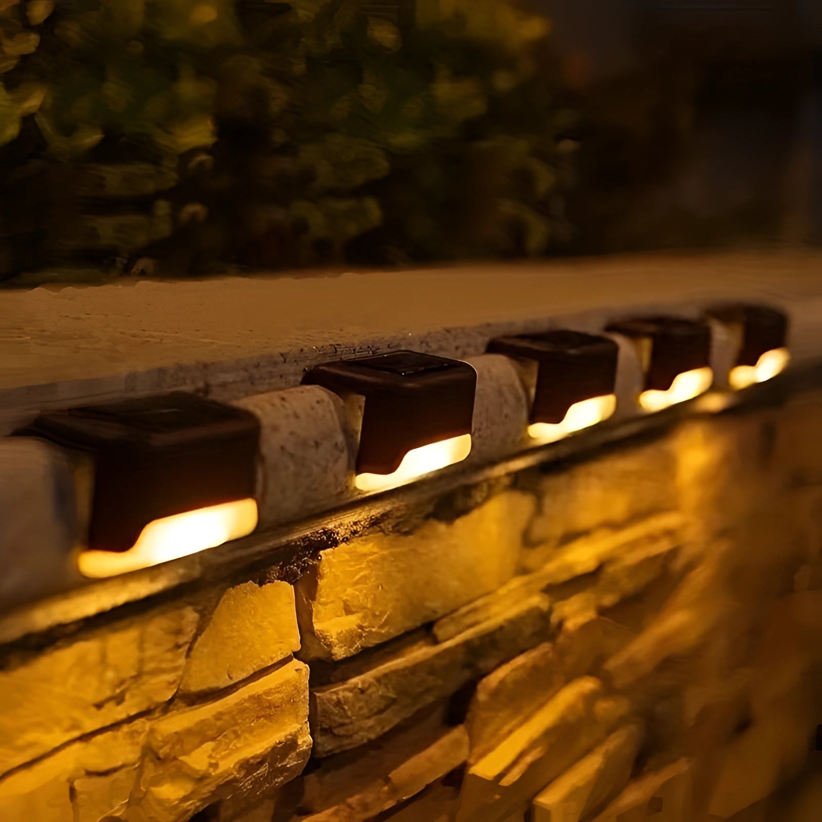 Energy-efficient LED waterproof deck lights installed on a brown wooden deck with a rectangular design, casting an amber glow against the brickwork, surrounded by grass and landscape at night.