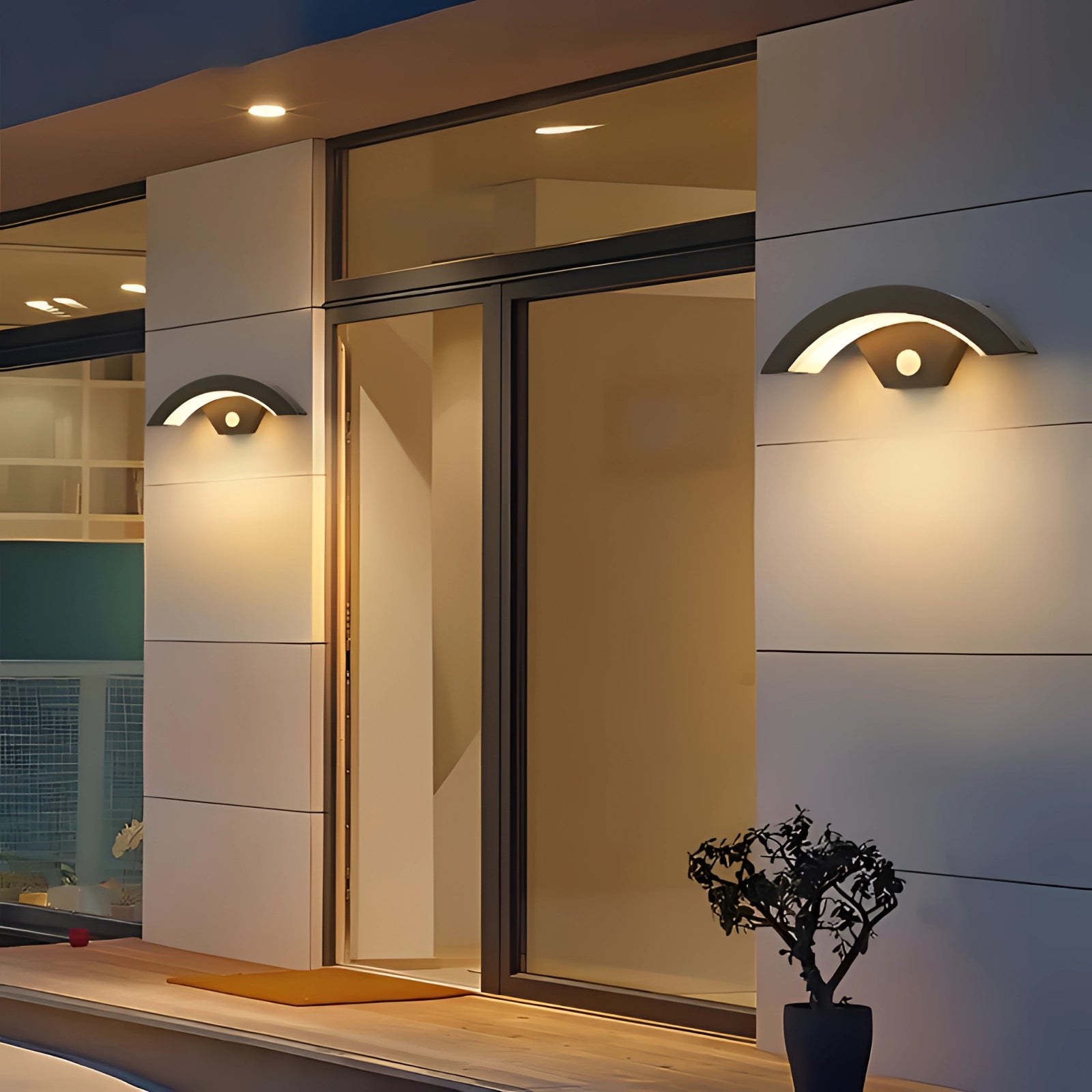 Modern outdoor lighting fixture shaped like an eye, mounted on a wall, illuminating the surrounding area with a soft glow. The sleek design enhances the architecture and complements the contemporary property setting.