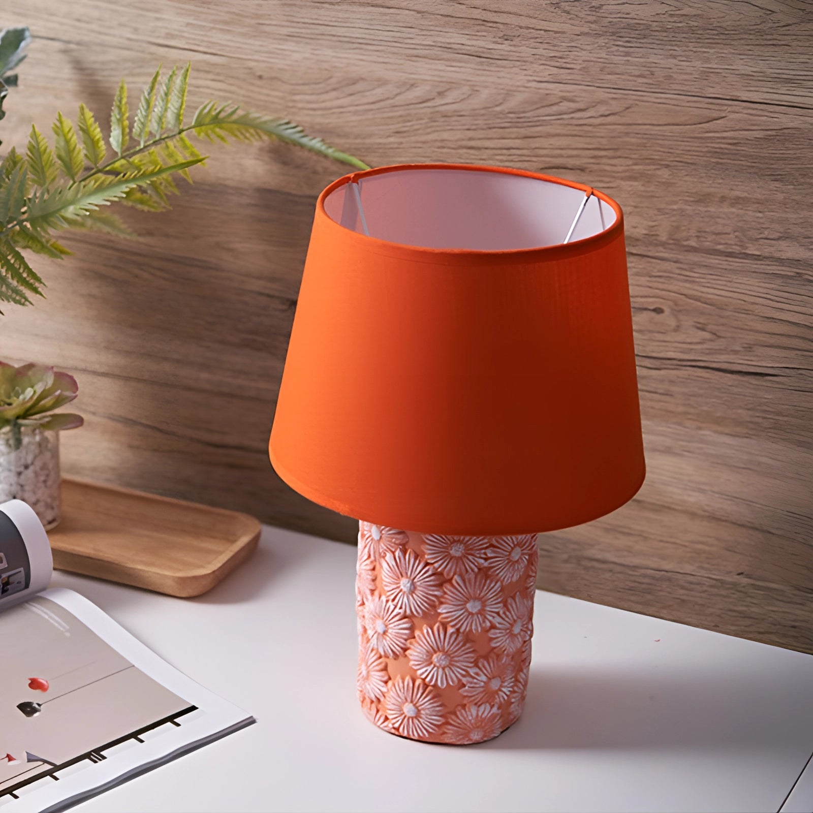 Floral ceramic table lamp with a sunflower base, featuring a warm peach tint, placed on a wooden table.
