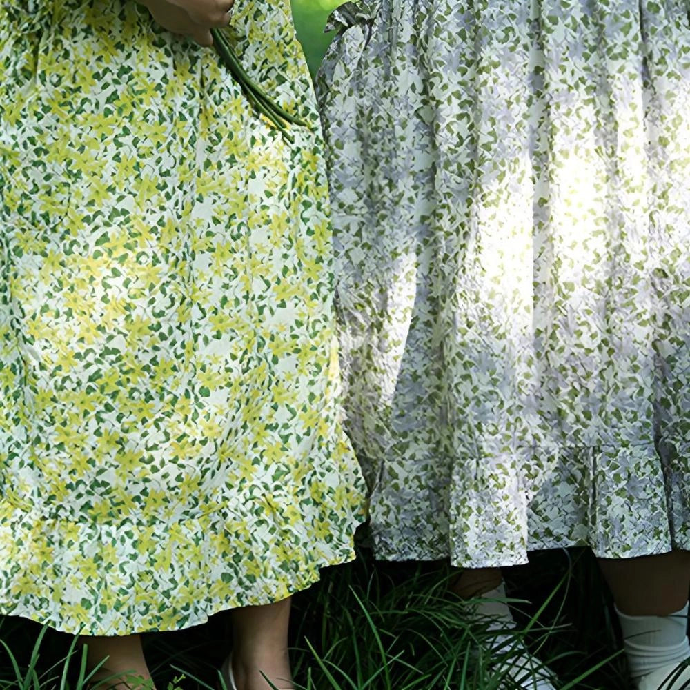 Floral cotton apron for women displayed on a table setting with a vintage kitchen theme, featuring a colorful floral pattern. The apron has pockets and is laid out on a tablecloth, surrounded by chairs and plants, giving a warm, homey feel.