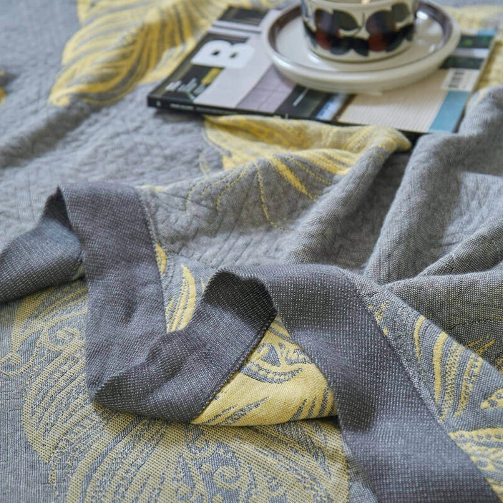 Floral yellow leaf pattern reversible blanket with grey bed linen decor, featuring a detailed pattern design displayed on a wooden surface.