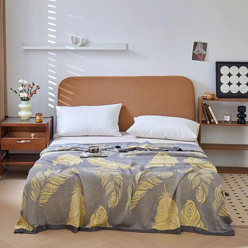 Floral yellow leaf pattern reversible blanket on a bed with grey bed linen decor, featuring a window and wooden bed frame in a cozy interior setting.