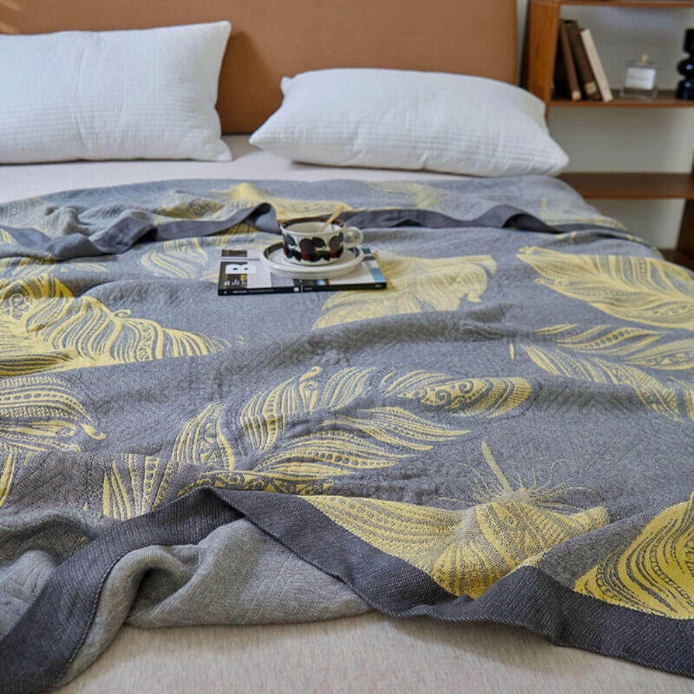Floral yellow leaf pattern reversible blanket with grey bed linen decor, displayed on a neatly made bed, showcasing its intricate design and soft texture.