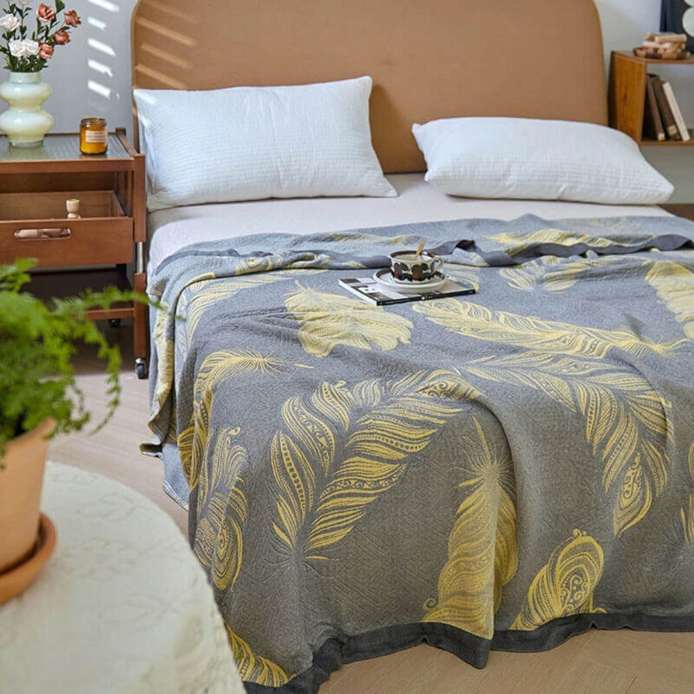A cozy grey bed features a reversible blanket with a vibrant floral yellow leaf pattern, enhancing the room's decor with a touch of elegance and comfort.