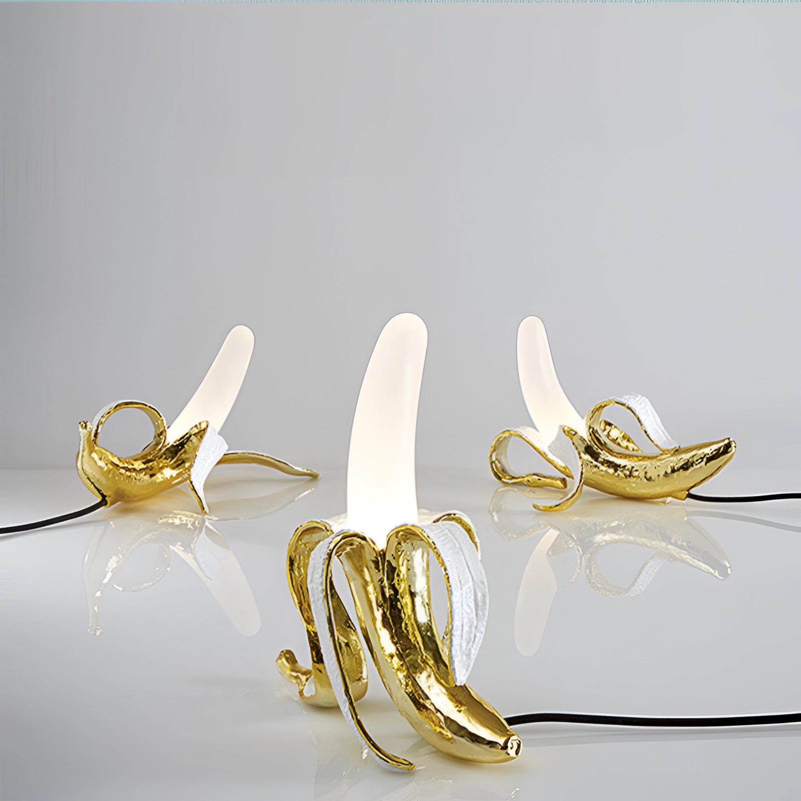 Gold banana-shaped table lamp made of resin, featuring a modern art design as a fruit sculpture. The lamp has a shiny metallic gold finish, adding a luxurious and artistic accent to any decor.