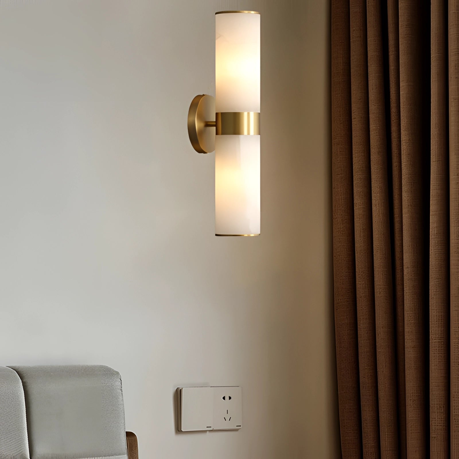 Gold bathroom sconce with a cylindrical frosted glass design mounted on a wall, shown in a modern interior setting.