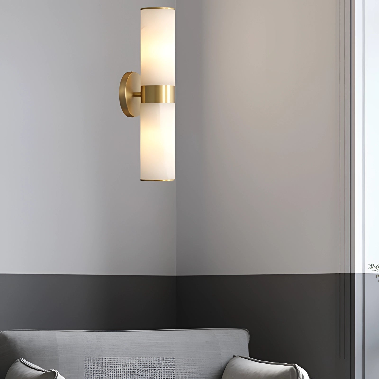 Gold bathroom sconce with a cylindrical frosted glass shade mounted on a rectangular base, illuminated and set against a stylish interior design backdrop.