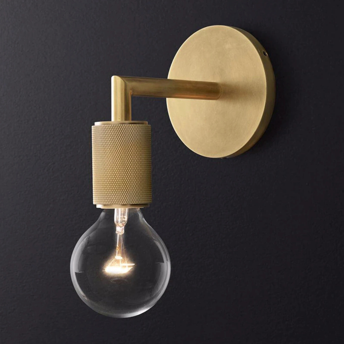 Gold brass wall sconce with geometric glass design and vintage bulb, mounted on wood background, industrial minimal style.