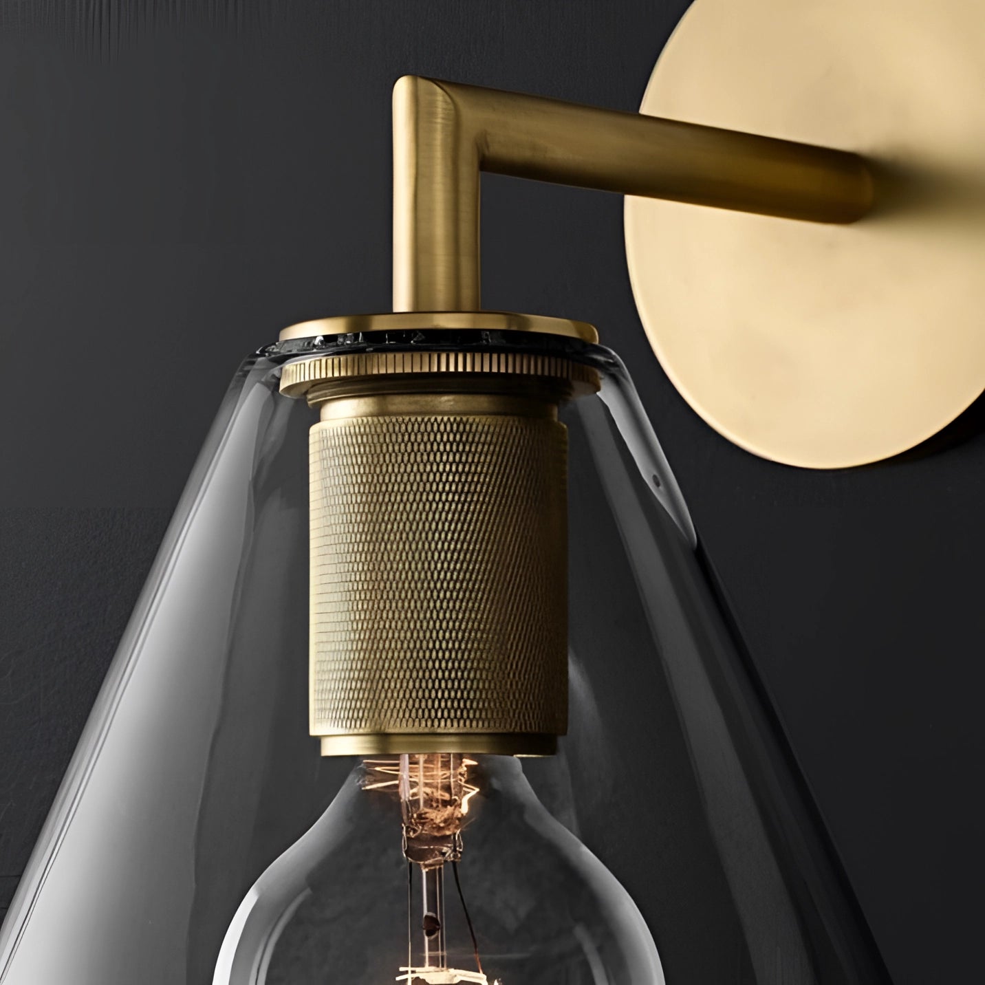 Gold brass wall sconce with a geometric glass design and vintage bulb, featuring an industrial minimal style, mounted on a wall.