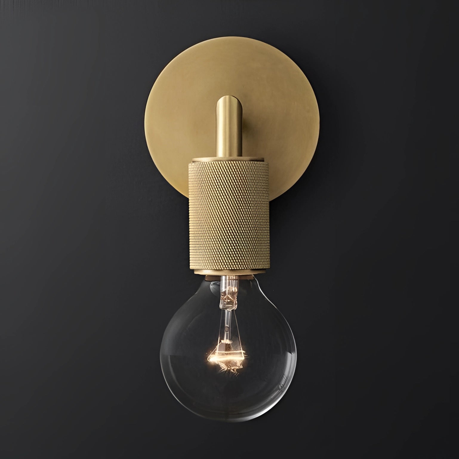 Gold brass wall sconce with geometric glass design, featuring a vintage bulb and simple armed structure, mounted on a wall in an industrial minimal style setting.