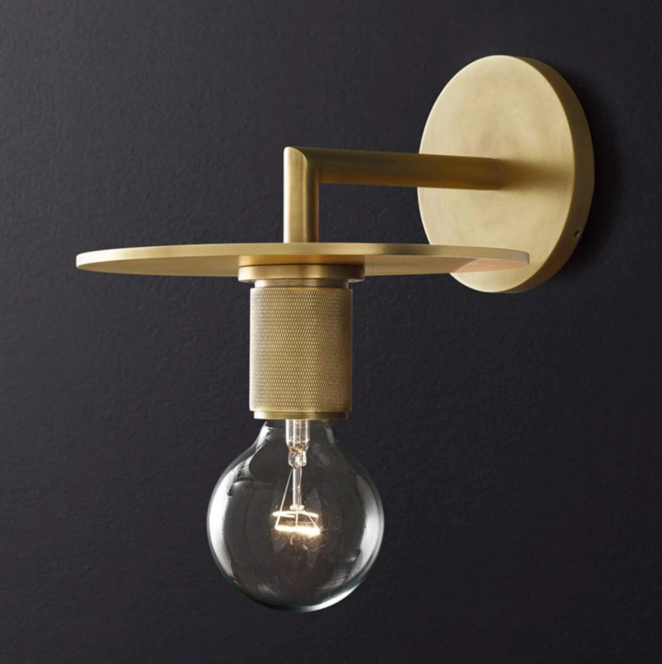 Gold brass wall sconce with geometric glass design and vintage bulb, mounted on a wooden wall with industrial minimal style elements.