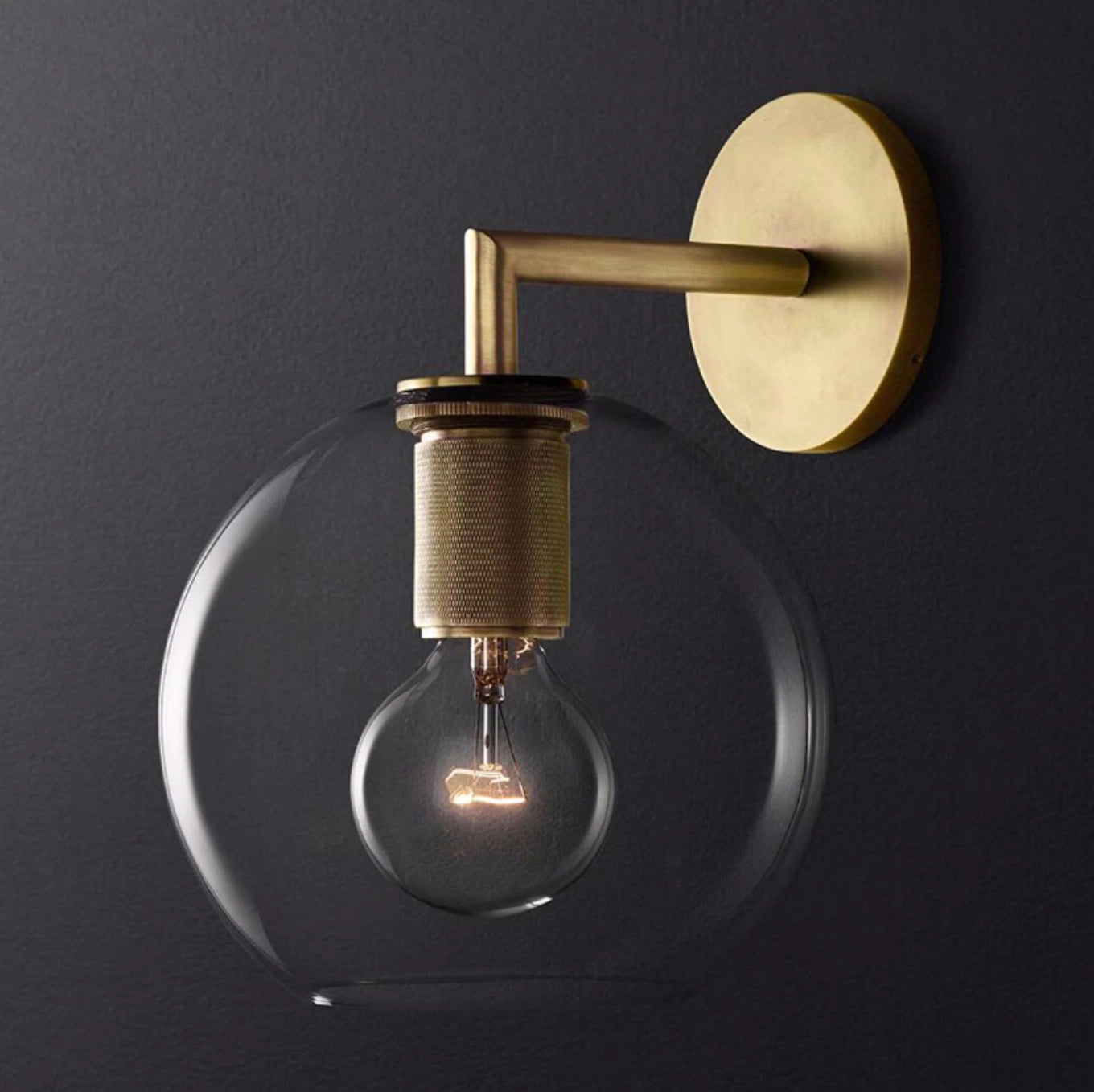 Gold brass wall sconce with geometric glass design, featuring a vintage-style bulb; industrial minimal aesthetics.