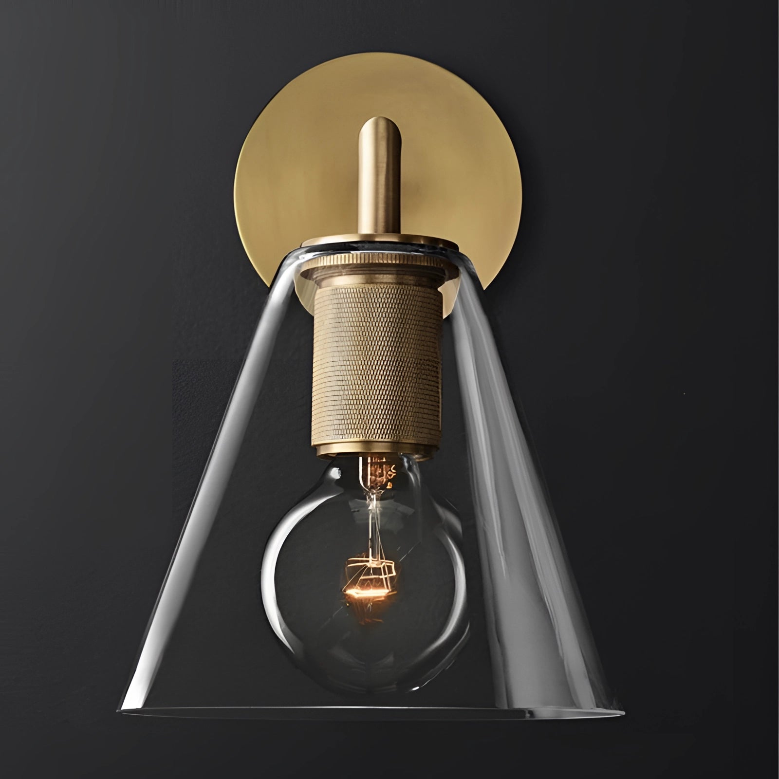 A gold brass wall sconce with a geometric glass design, vintage bulb, and industrial minimal style, featuring a classic armed structure.