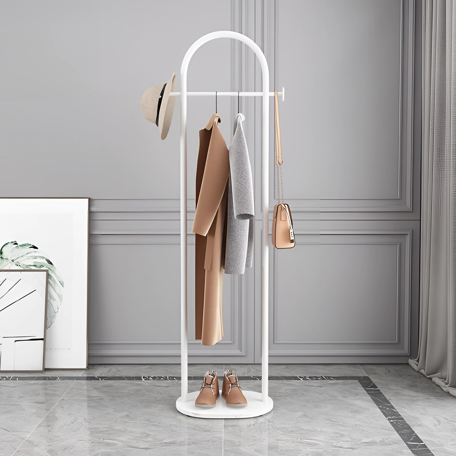 Gold metal coat rack with marble base in a minimalist design, positioned in a room with white interiors and wooden flooring. The luxurious hanger complements the modern, sophisticated fashion design of the space.