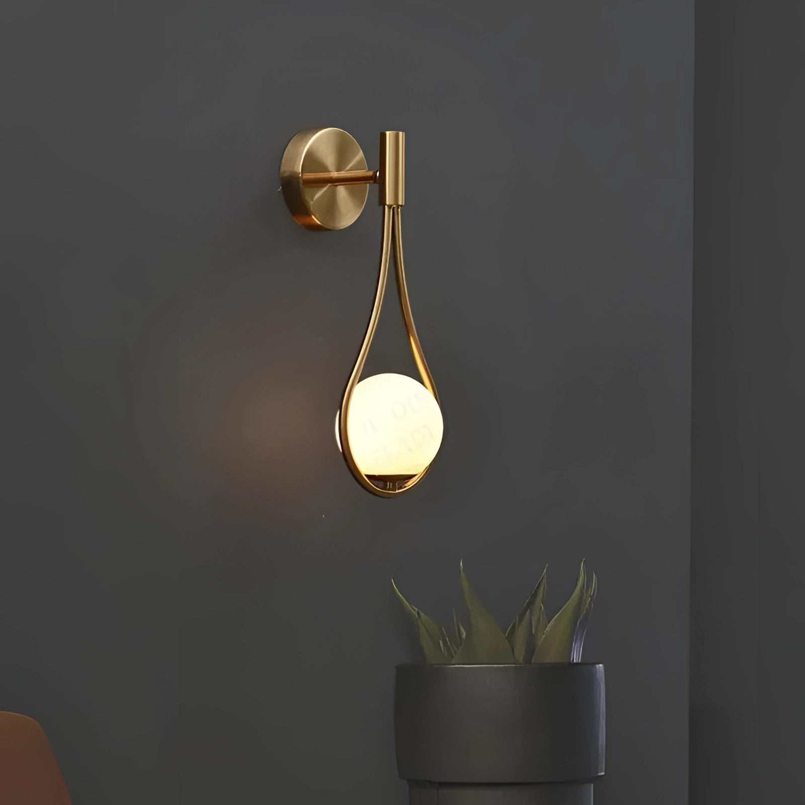 Gold wall-mounted luxury soap dispenser in a modern bathroom setting, surrounded by decorative elements including a houseplant and wooden accents.