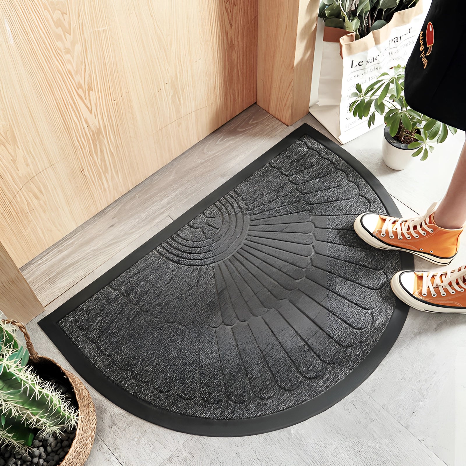 Gray semi-circular non-slip door mat placed on a wooden floor, measuring 60 x 90 cm, with interior elements such as plants in the background.