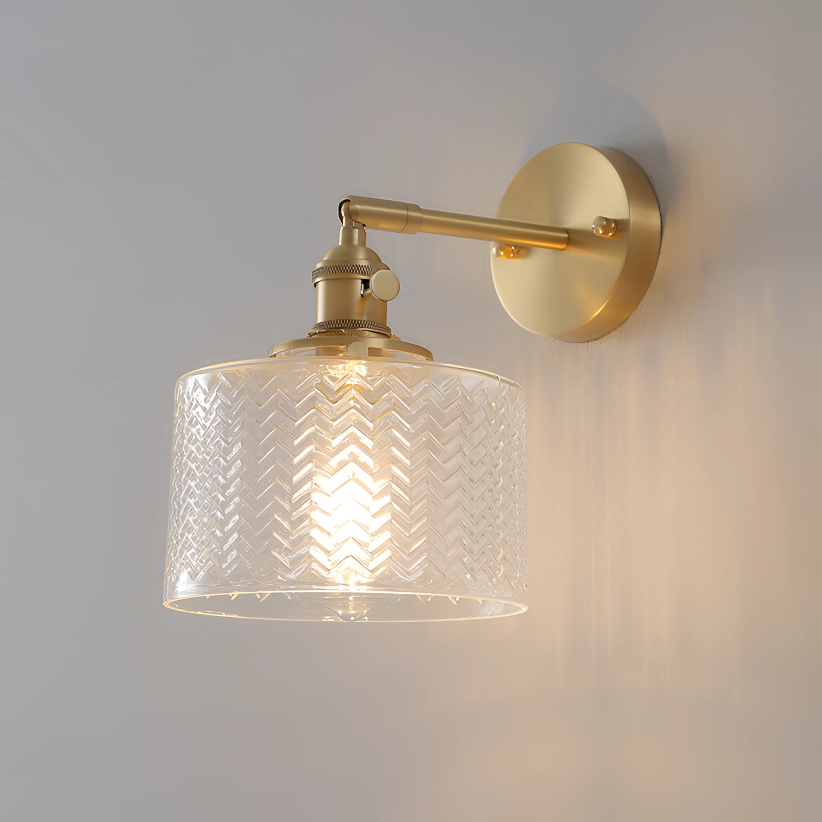 Green chevron wall lamp with a brass sconce featuring a geometric pattern, shown with a clear shade.