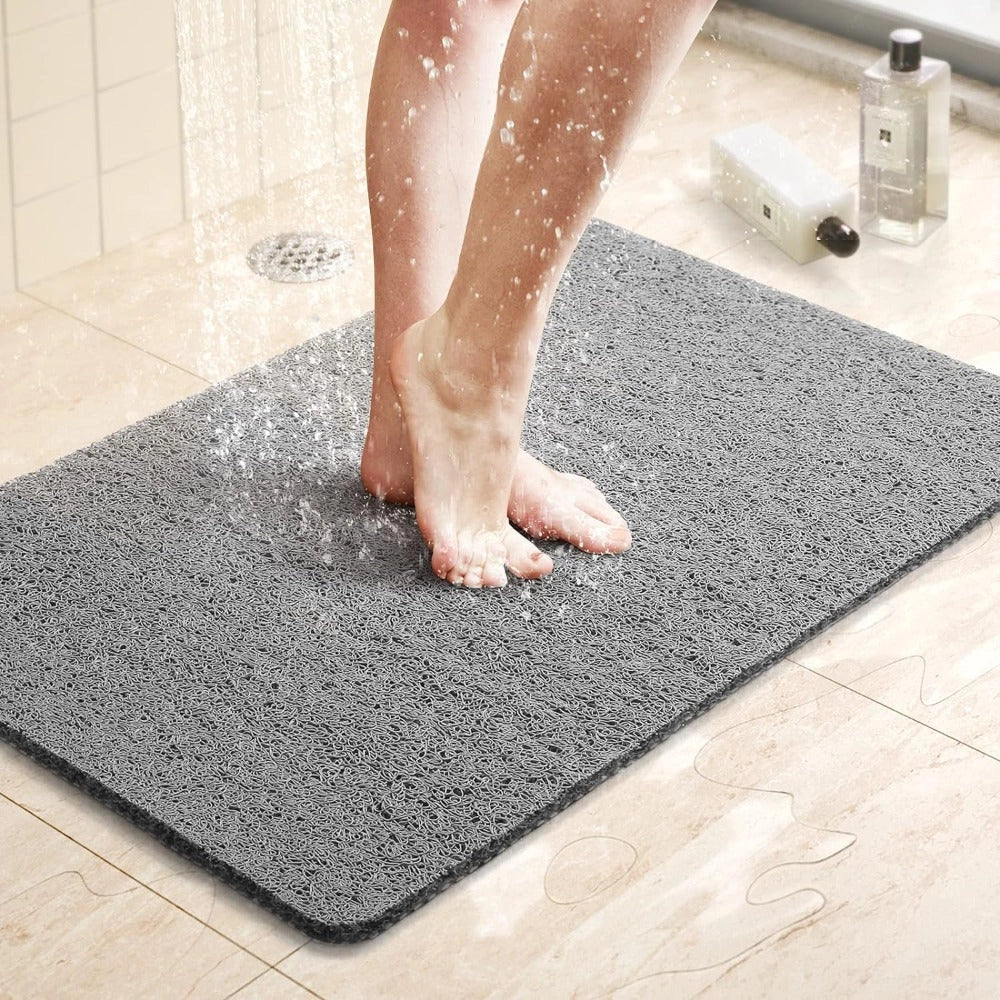 Grey non-slip quick-dry microfiber bathroom mat on a wooden floor, showing a person standing barefoot with visible legs and calves.