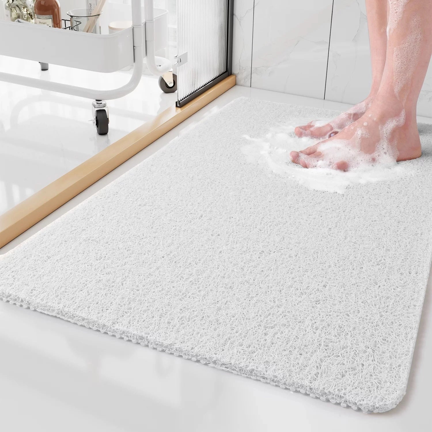 White extra-large rectangular bathroom mat made of quick-dry microfiber material placed on a hardwood floor near a plumbing fixture. A human foot is partially visible, highlighting the mat's non-slip feature.