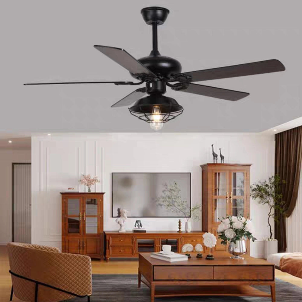 Industrial black ceiling fan with light and remote control, featuring a vintage outdoor design, mounted on a wooden ceiling in a stylishly furnished interior space with plants and picture frames.