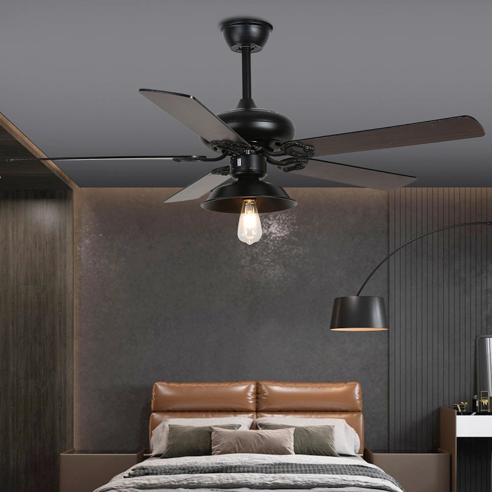 Industrial black ceiling fan with light and remote, featuring a vintage outdoor design, installed on a wooden ceiling with a warm brown finish. The fan is part of a cozy and comfortable interior setting, providing efficient lighting and air circulation.