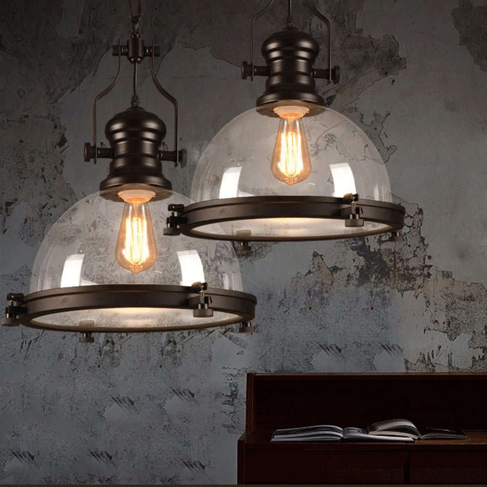 Industrial black iron pendant light with a frosted glass dome, featuring a retro adjustable design. The pendant light is illuminated with a warm amber glow.