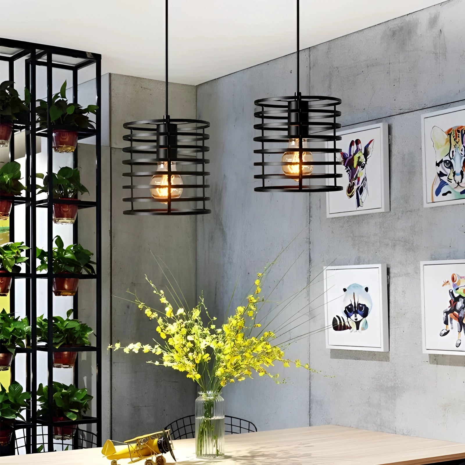 Modern black industrial cage pendant light hanging from the ceiling in a minimalist interior setting with a large window, potted plant, and wall in view.