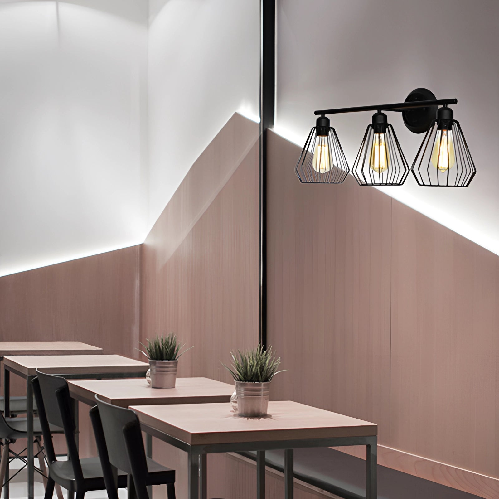 Industrial geometric metal cage pendant light with an Edison bulb, hanging above a wooden table in a modern interior setting, complemented by a plant and stylish decor elements.