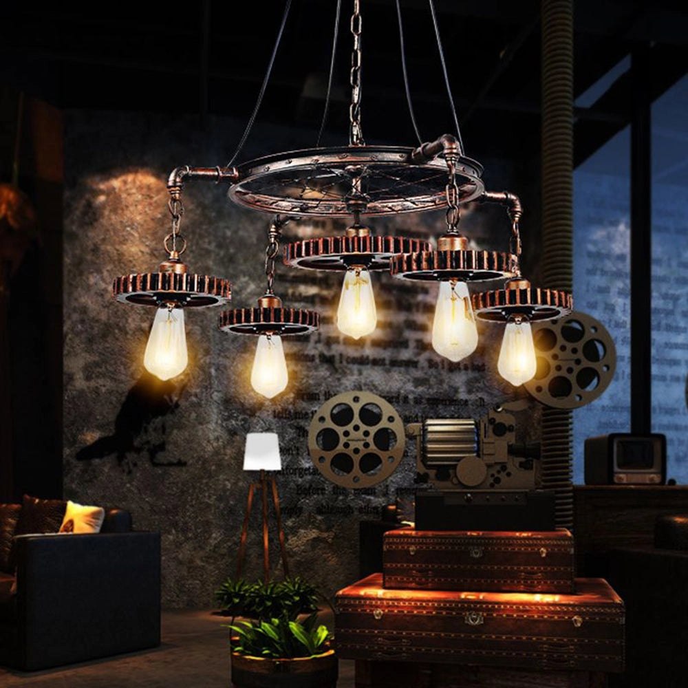 Industrial steampunk chandelier with vintage gear design featuring triple Edison bulbs, displayed with five lights in antique bronze finish, hanging in a tastefully decorated interior setting with plants and decorative elements.