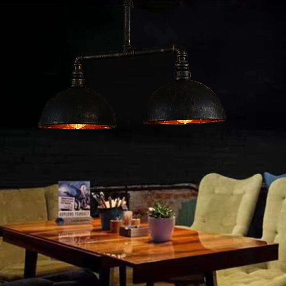 Industrial vintage pipe dual dome black metal pendant light hanging above a wooden coffee table in a living room setting with stylish interior design elements, including a houseplant and hardwood flooring.