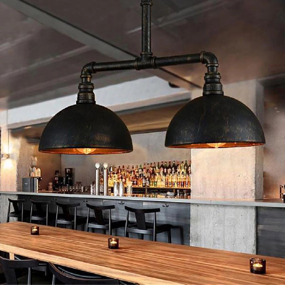 Industrial vintage pipe dual dome black metal pendant light hanging above a wooden kitchen countertop with bottles and barware, showcasing an interior design that combines rustic and modern elements in a cozy setting.