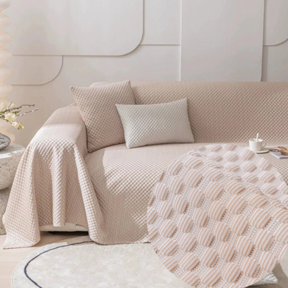 Light blue quilted anti-slip sofa cover draped over a beige studio couch in a living room setting, highlighting its pet-friendly, washable design. The cover is rectangular, enhancing comfort and style in the interior space.