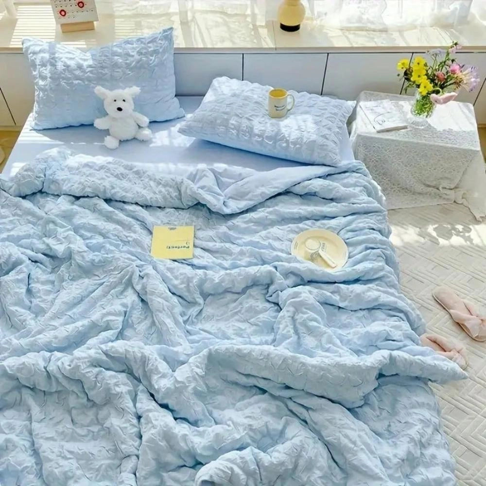 Light blue ruffled comforter set with a plush and textured design, displayed on a bed with matching pillows in a cozy bedroom setting featuring white and grey tones, with a hint of aqua and wood accents.