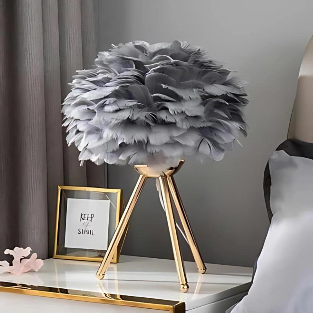 Luxurious grey feather table lamp with a modern design featuring a gold tripod base, situated on a table in an elegantly styled interior.