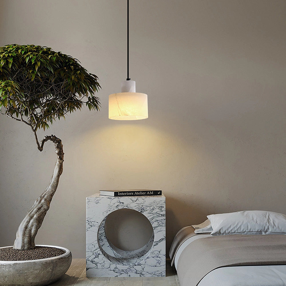 A luxury alabaster pendant light with a natural stone finish, suspended from the ceiling in a minimalist interior featuring wooden accents, a grey floor, and a touch of greenery from a nearby plant.