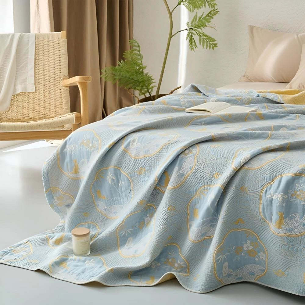Luxury blue bedding set with ornate gold floral pattern displayed on a wooden bed frame in a stylishly decorated interior room.