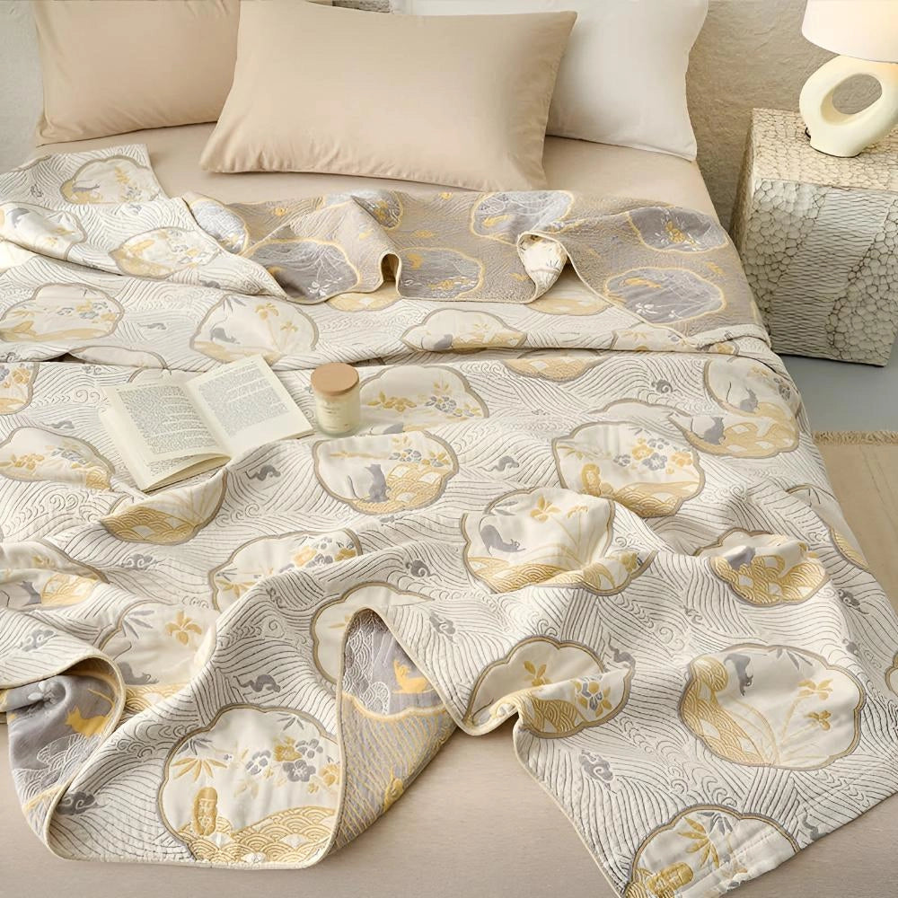 Luxury blue bedding set featuring an ornate gold floral pattern, displayed on a well-made bed in a softly lit bedroom with beige wooden flooring.