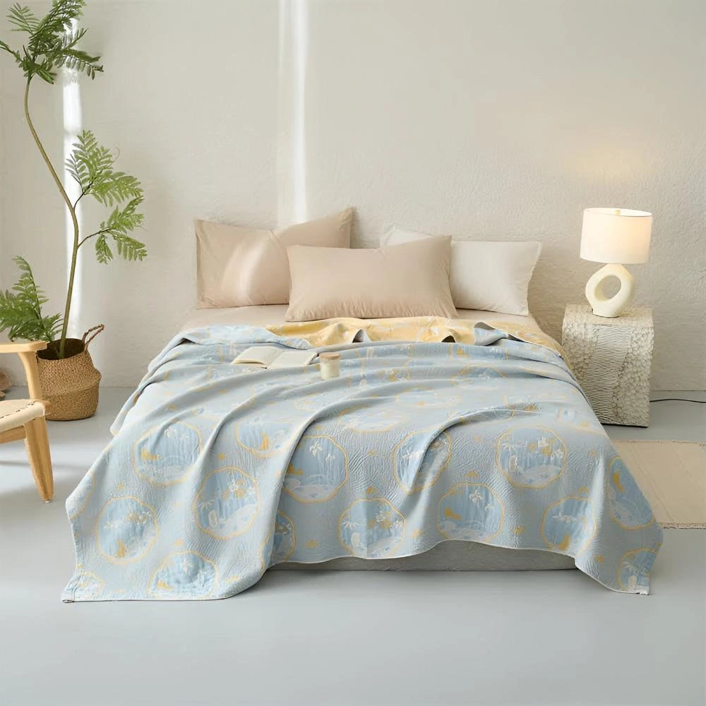 Luxurious blue bedding set adorned with an ornate gold floral pattern, featuring plush pillows on a wooden floor, surrounded by houseplants and elegant interior design elements.