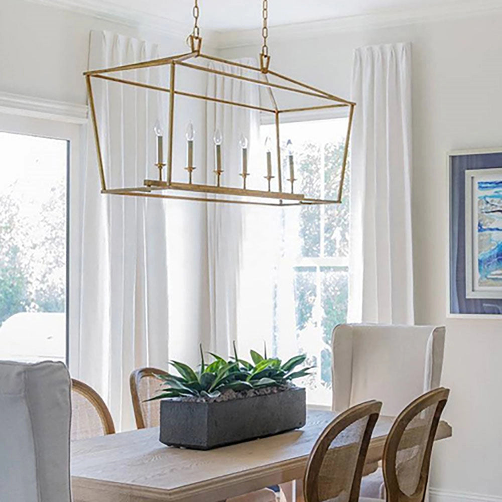 Luxury brass LED geometric pendant chandelier in gold with 6 lights, hanging in a stylish living room with modern interior design elements, featuring wooden furniture, large windows, and decorative plants.