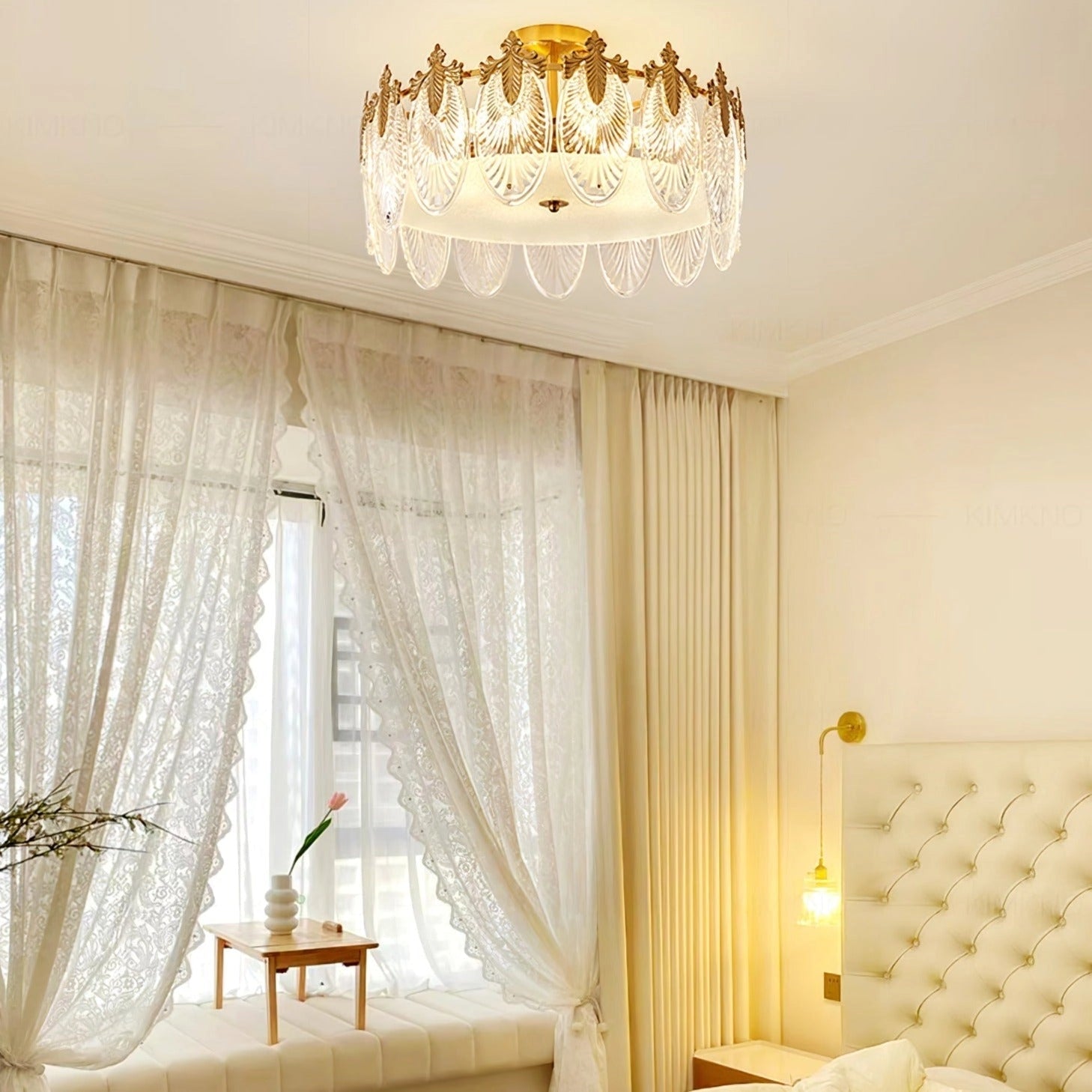 Elegant gold leaf vintage luxury crystal chandelier mounted on a ceiling, illuminating a sophisticated interior space with white walls, wooden accents, and decorative elements such as curtains and plants.