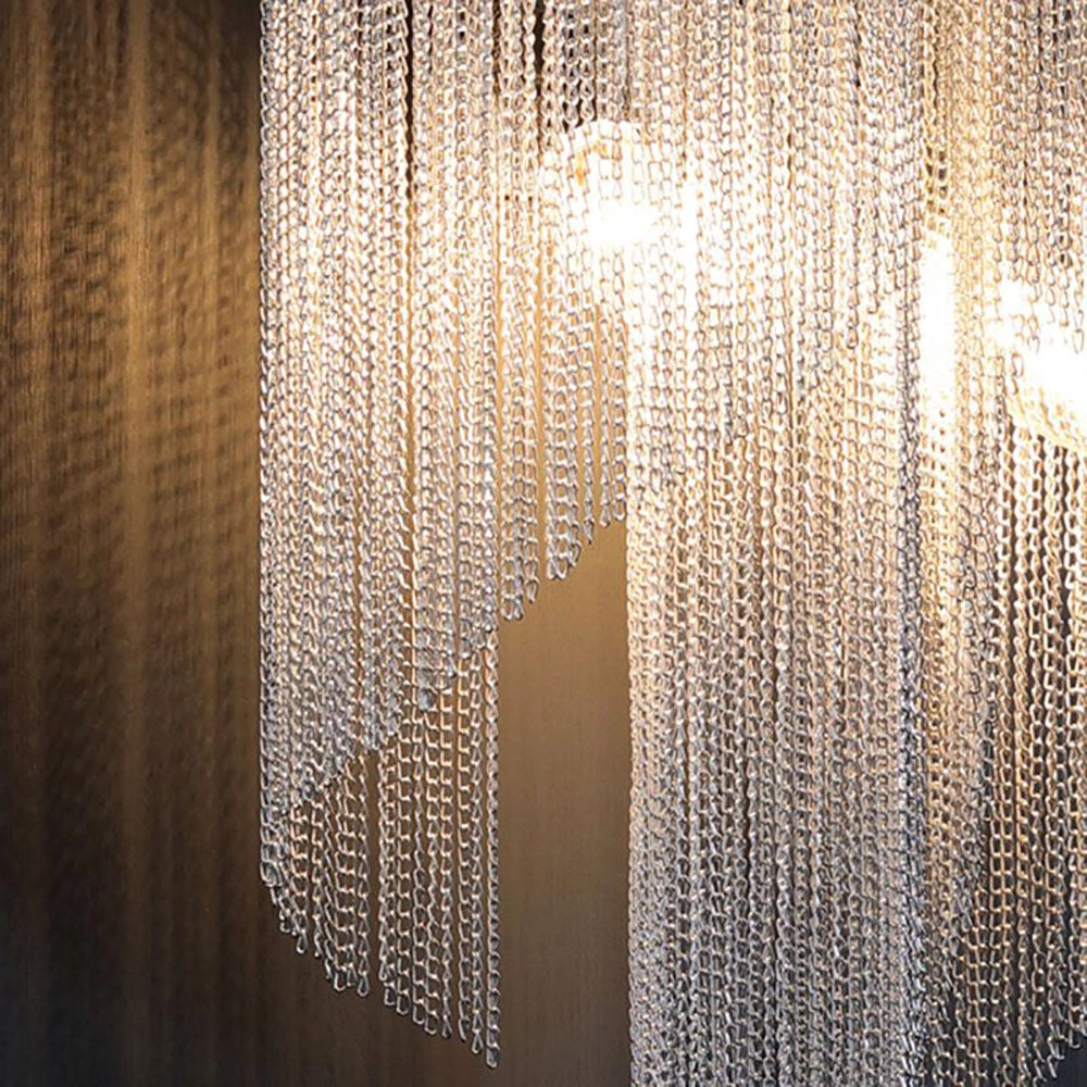 Luxury crystal wall sconce with contemporary chain drape design, mounted on a brown wooden base and set against a grey, textile-patterned wall in a stylish interior space.