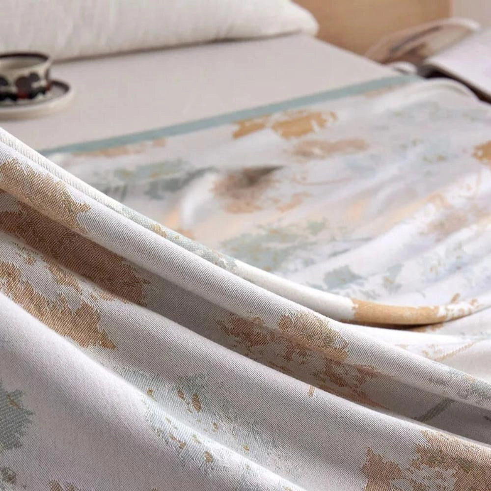 Luxurious floral silk comforter draped over a beige couch, showcasing a sophisticated pattern in a soft grey and beige palette, surrounded by elegant decor elements that enhance the cozy and stylish ambience.